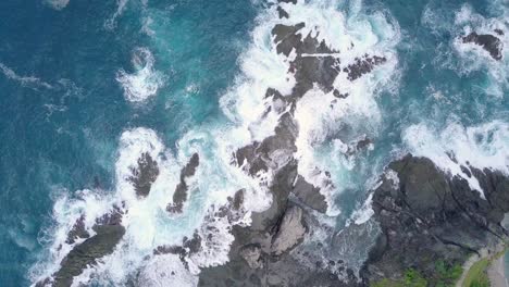 aerial overhead shot of waves of indian ocean hitting boulder and rocks of siung beach in sunlight - indonesia island,asia