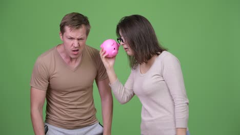 young couple shaking piggy bank together against green background