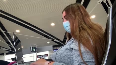 Junge-Langhaarige-Frau-Mit-Coronavirus-maske,-Die-In-Der-Flughafenlounge-Am-Laptop-Arbeitet