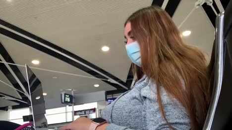 mujer joven de cabello largo con máscara de coronavirus trabajando en una computadora portátil en el salón del aeropuerto