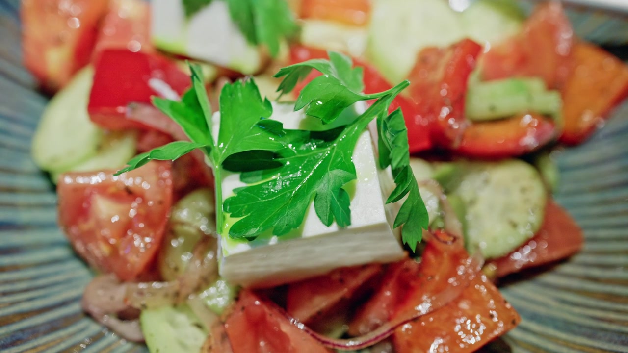 Nærbillede af en middelhavsinspireret salat med friske agurkeskiver, modne tomatstykker, rødløg og tern af fetaost, toppet med persilleblade