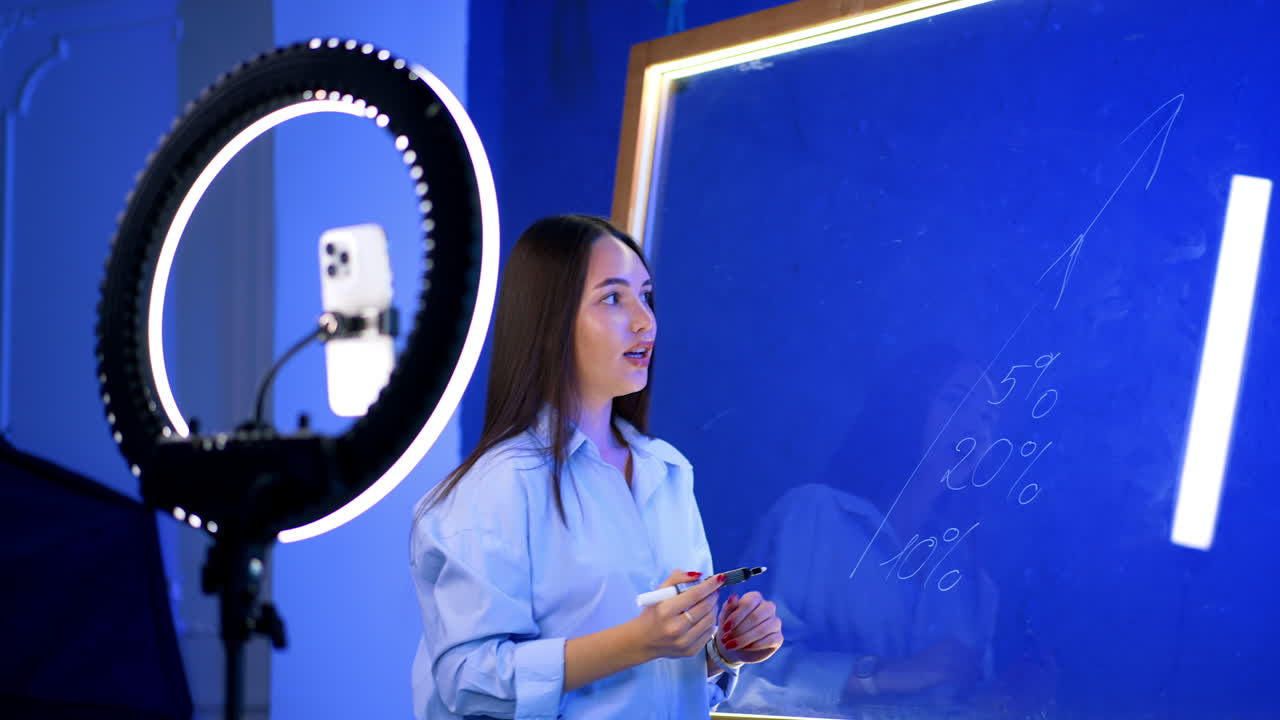 Young woman creating art in studio space. A young woman writes creatively on a blue canvas inside a well-lit studio, surrounded by art supplies and equipment
