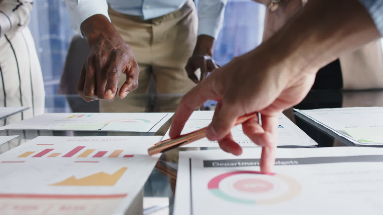 Pointing at business reports and charts, team discussing project in office meeting