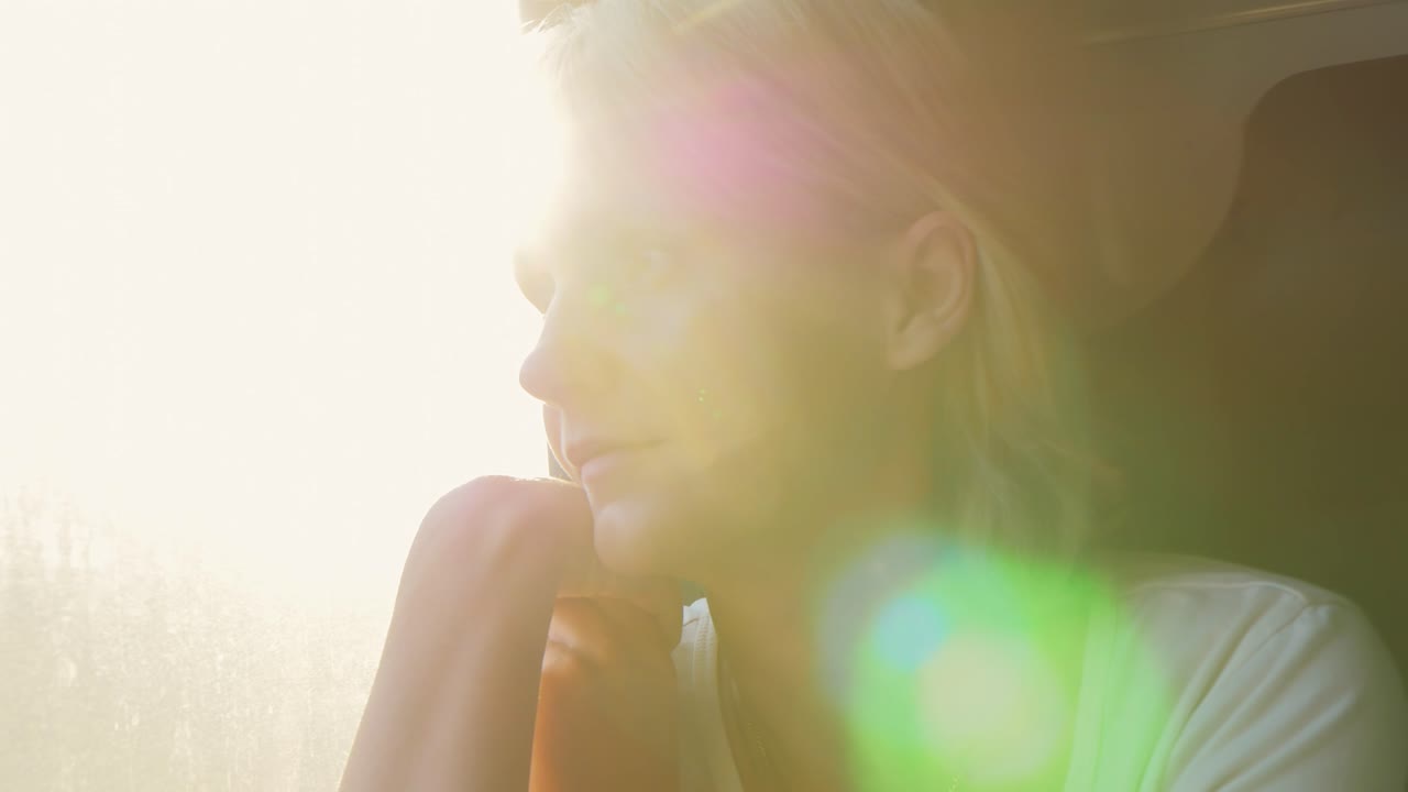 портрет молодой женщины, едущей в поезде, которая смотрит в окно, солнечные лучи освещают ее