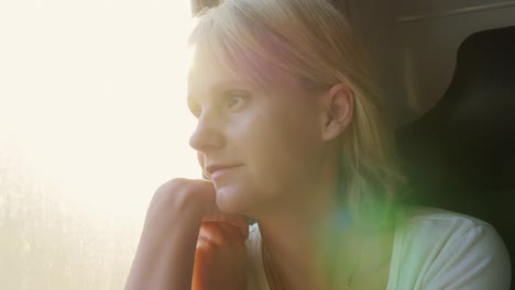 portrait of a young woman traveling in a train looking out the window the sun's rays illuminate her