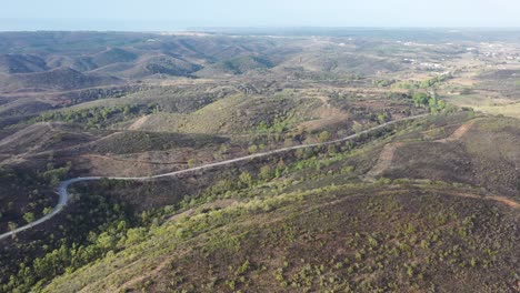 Winding-road-approaching-Tonel-Beach-in-southwest-Portugal-with-car-traffic,-Aerial-pan-right-shot