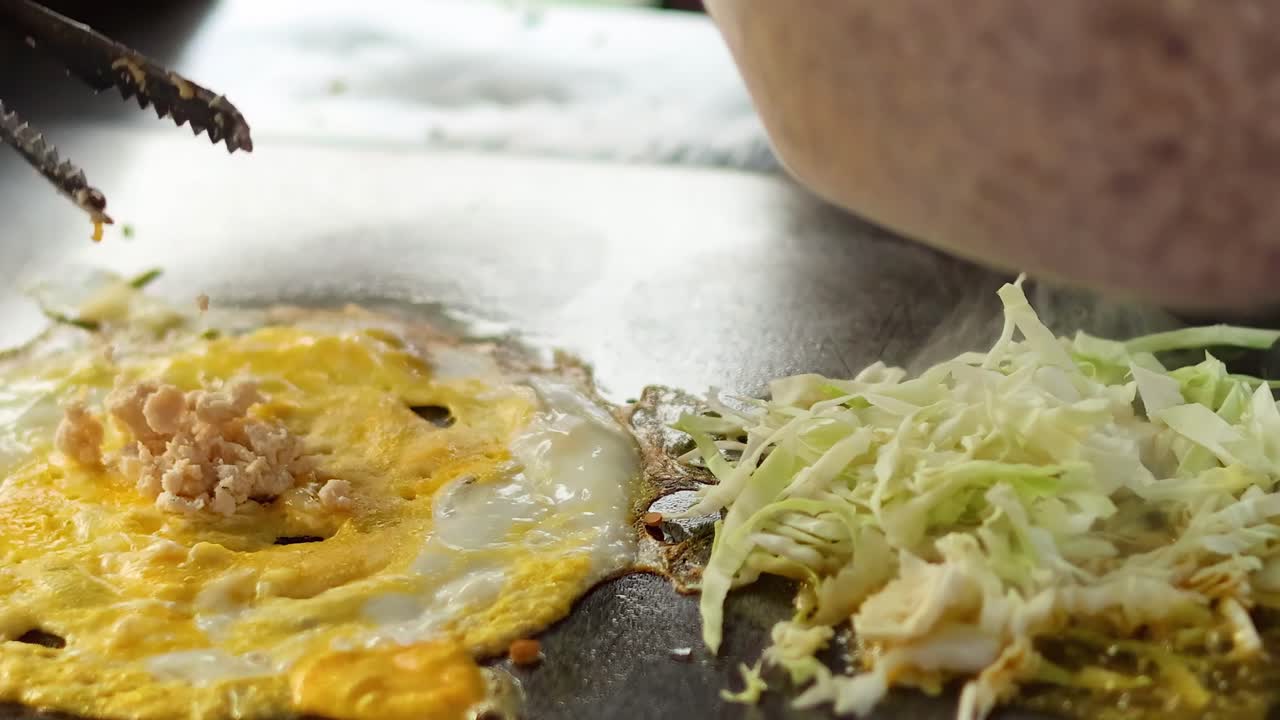 Close-up of egg and cabbage being cooked on a griddle with added minced ingredients.