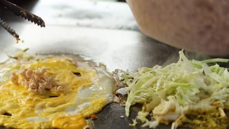 close-up of egg and cabbage being cooked on a griddle with added minced ingredients.