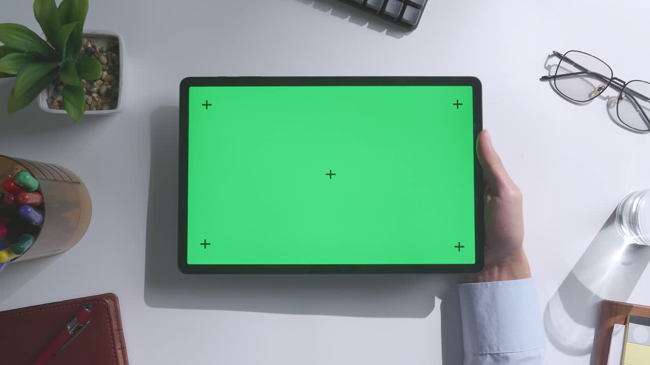 верхний вид ноутбука с макетным зеленым экраном chromakey на деревянном офисном столе рядом с ноутбуком с ручками, очками и стаканом воды.