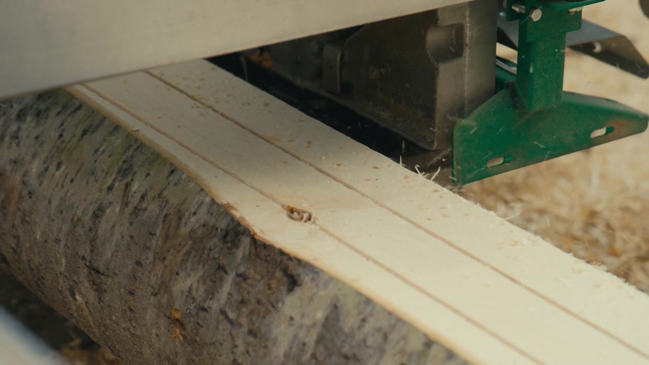 Un primo piano al rallentatore mostra assi fresche tagliate direttamente da un tronco in una segheria portatile all'aperto, catturando la lavorazione del legname grezzo, la consistenza ruvida e la produzione di legno su piccola scala.