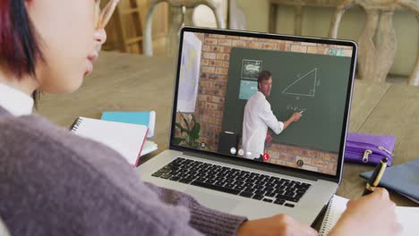 Asian female student using laptop for online lesson with caucasian male teacher on screen
