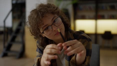 Retrato-De-Una-Estudiante-Feliz-Con-Cabello-Rizado-Y-Gafas-Leyendo-Un-Libro-En-La-Biblioteca.