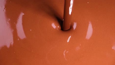 a focused view of chocolate being poured, creating ripples and reflections on a smooth surface.