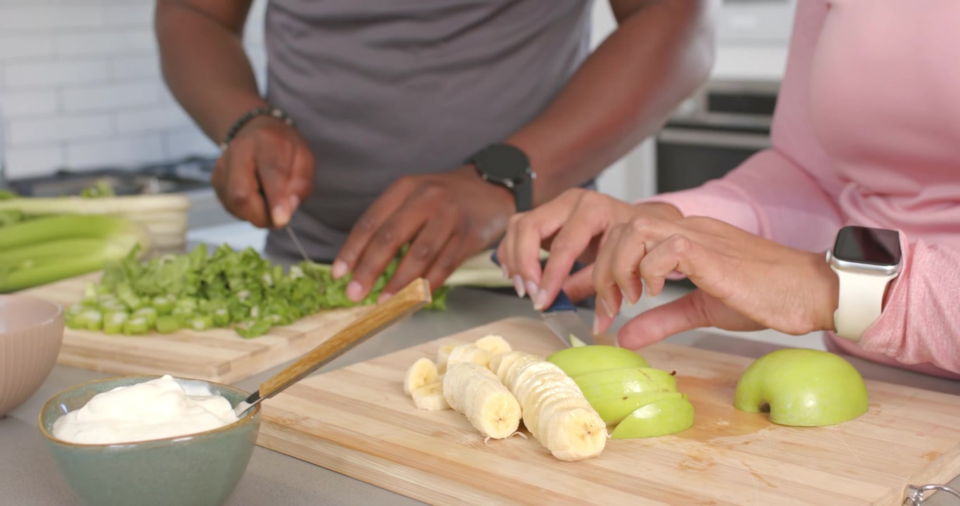 Incoraggiati dalla frutta sul tagliere, una coppia afroamericana taglia verdure e affetta mele per uno spuntino.