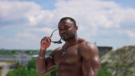 waist up portrait view of the strong stylish man wearing glasses while posing on clear blue sky background. shirtless bodybuilder showing his muscles