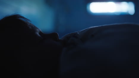 tired child lying back onto pillow to sleep in dark room, closeup profile view