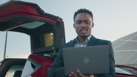 businessman using a laptop next to an electric car