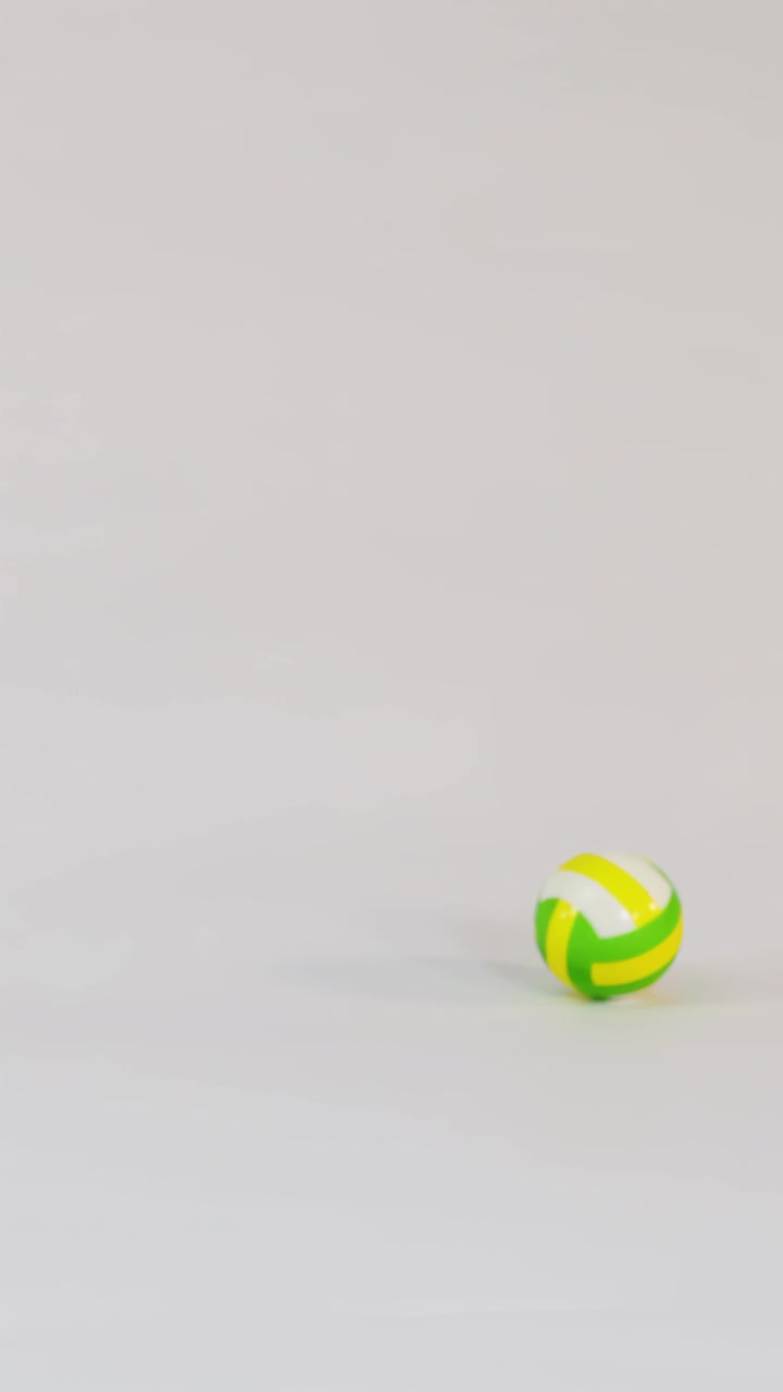 A small yellow and green volleyball bounces across a bright white studio floor in slow-motion