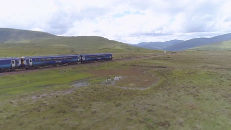 toma de seguimiento aéreo de un tren de cercanías que se dirige a través de rannoch moor