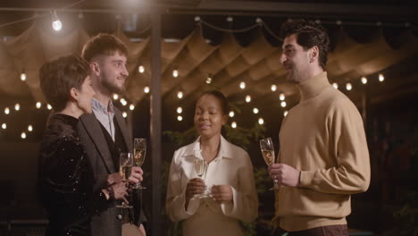 group of four multiethnic friends holding champagne glasses and talking to each other at the new year's eve party