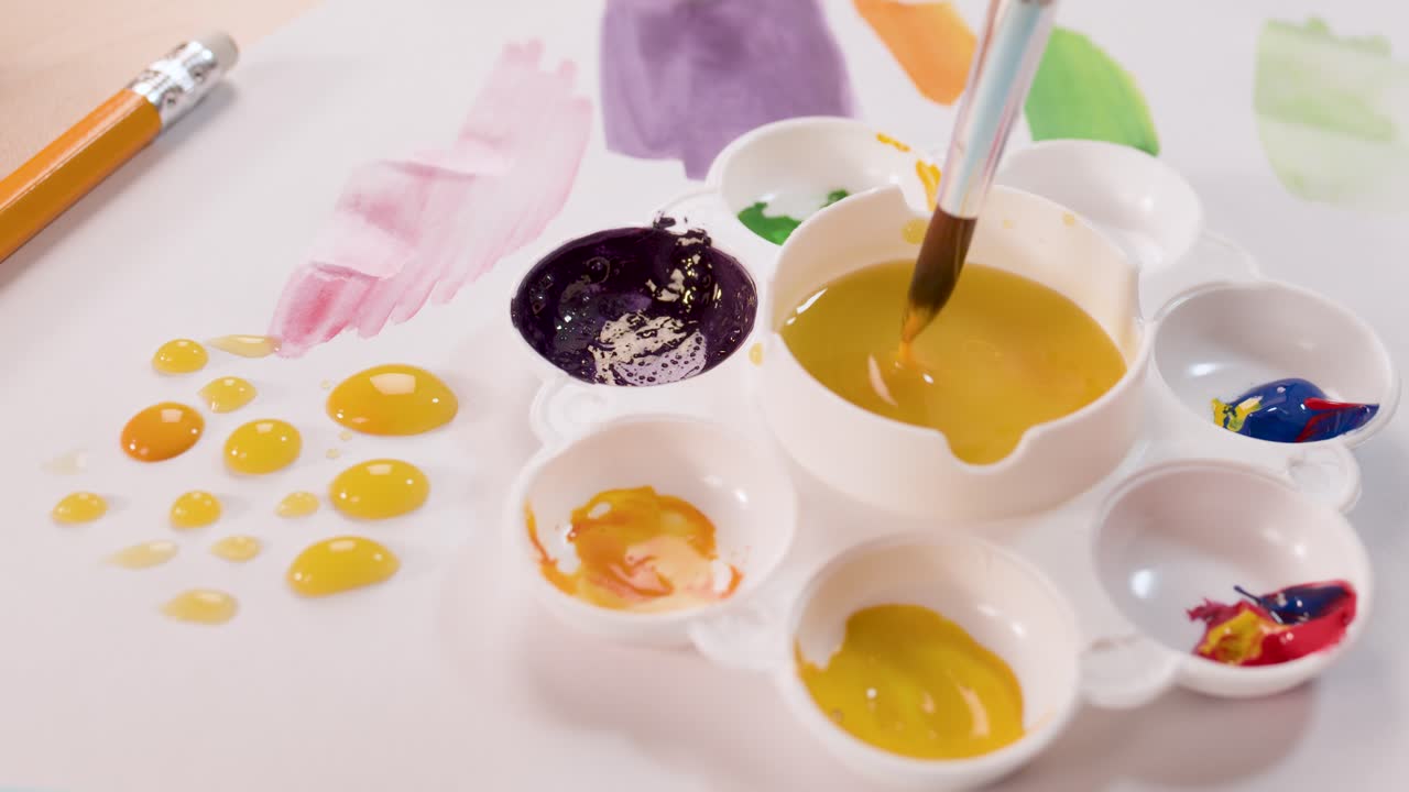 Child uses brush to mix yellow paint in palette, creating colorful dots on white paper