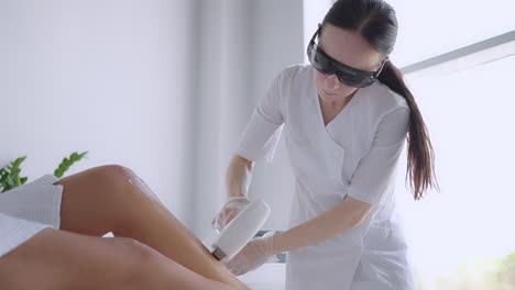 beautician doctor doing elos hair removal depilation on attractive young woman legs. woman legs getting pulses of laser light destroy hair follicle. laser hair removal procedure beautician salon.