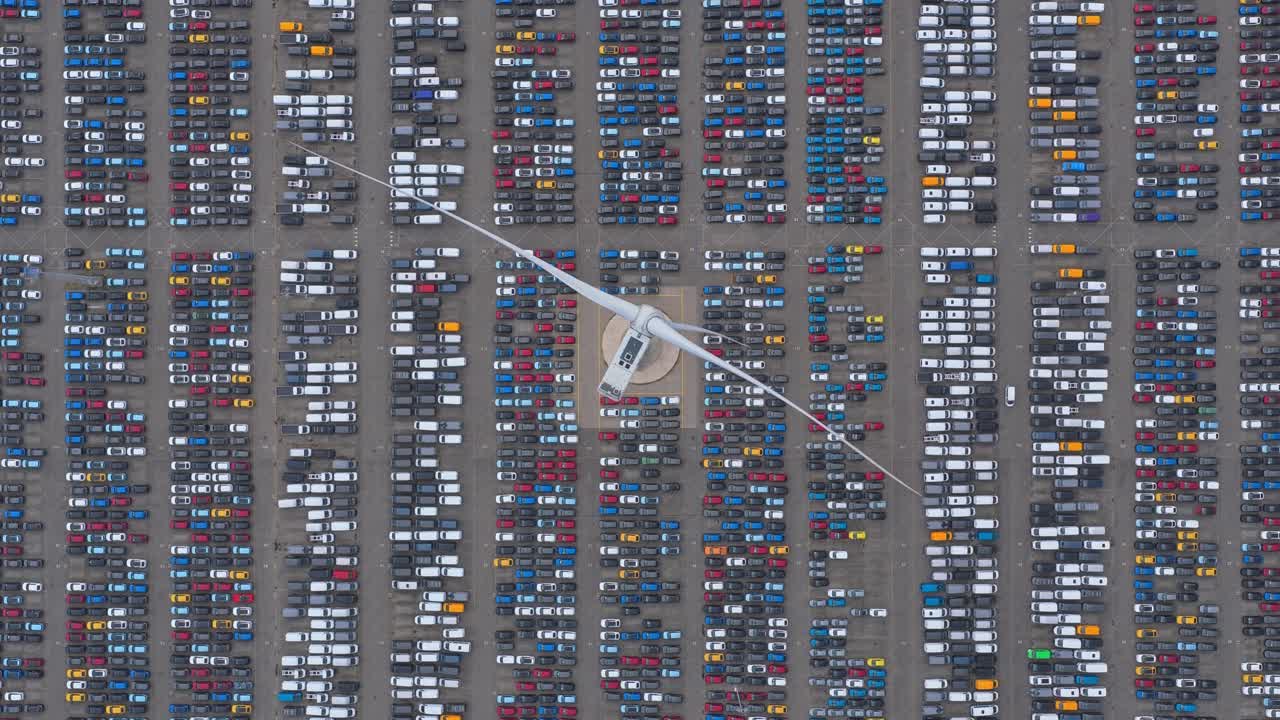 Drone shot of global auto yard with vehicles and wind turbine turning