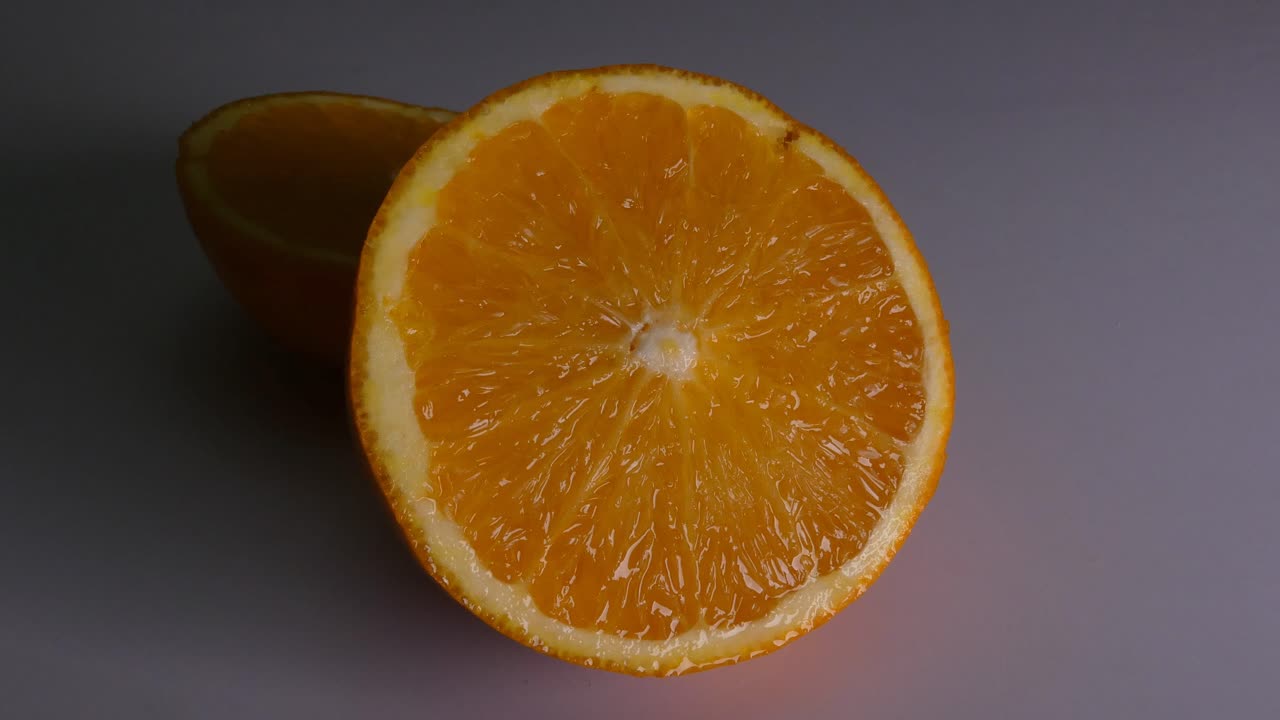 A sliced orange on a white background. The light source above the fruit moves slowly above it, slightly moving the shadows.