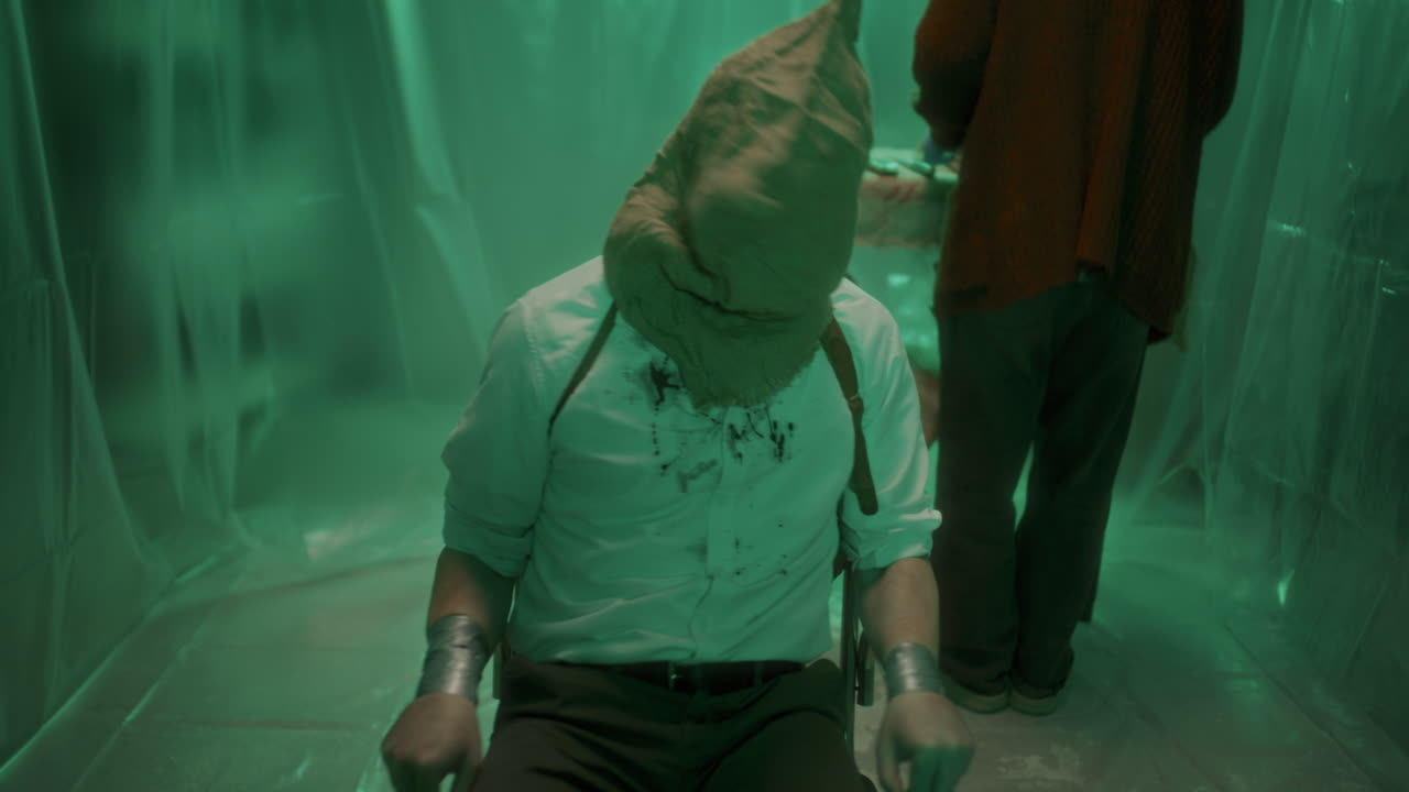 víctima aterrorizada con camisa ensangrentada, atada a una silla, tratando de escapar del asesino en serie