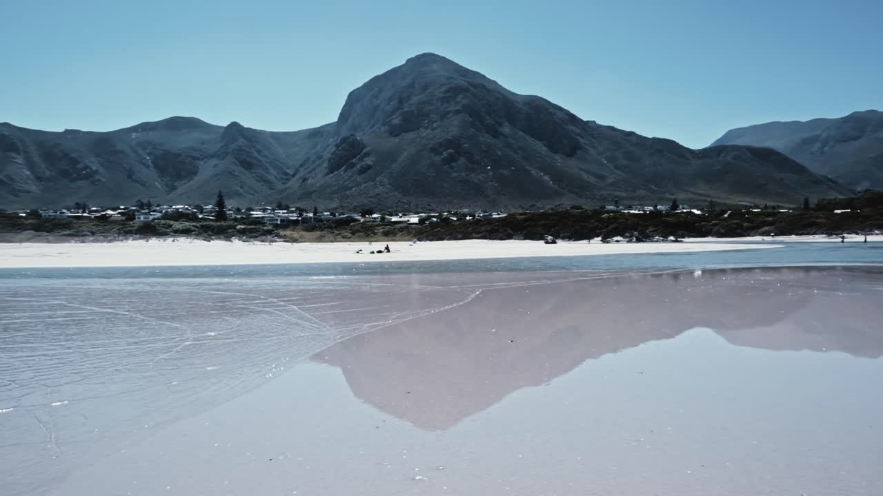 las montañas se reflejan en la arena húmeda en una playa en hermanus, sudáfrica.