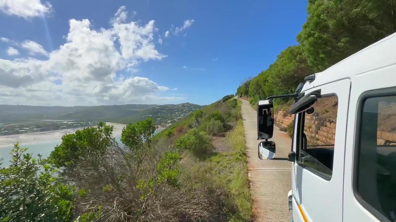 Veicolo turistico percorre una strada costiera con vista sulla laguna di Knysna e sulla baia di Featherbed in Sudafrica