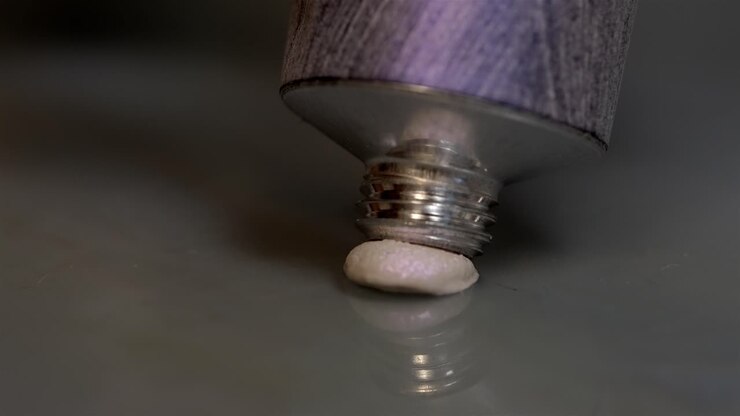 Metallic tube of oil paint squeezing out cream colored paint, closeup