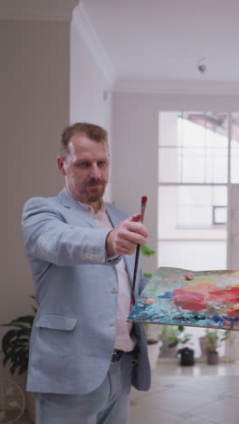 hombre barbudo inspecciona los resultados de la pintura en el caballete. artista profesional examina el lienzo para evaluar el fruto de los esfuerzos creativos en el estudio de arte moderno