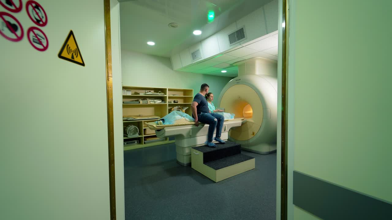 Male patient coming into the room with modern mri machine. Female medical worker near the modern magnetic resonance imaging scan in clinic.