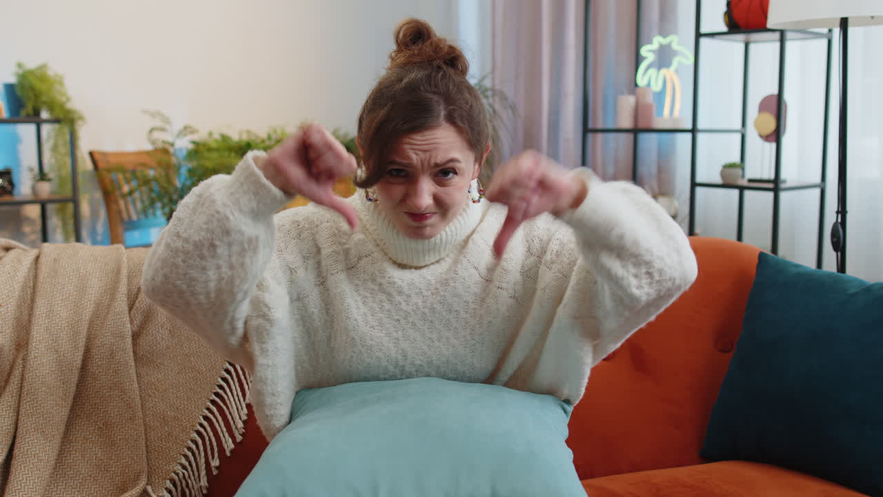 Upset young woman showing thumbs down dislike bad work disapproval dissatisfied feedback at home