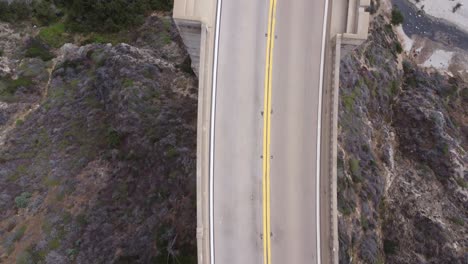 A bird's eye view of a bridge between two mountains with cars driving.