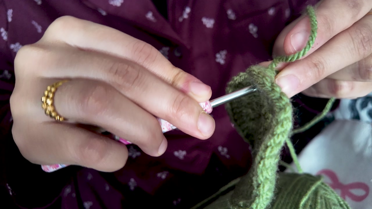 Hands working with a crochet hook and green yarn, creating textile fabric. slow motion