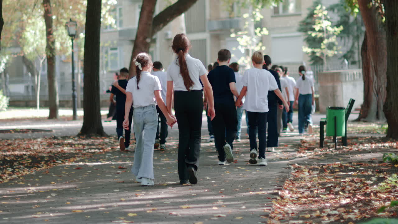 Group of school children strolling under green trees in a sunny park in Chisinau, Moldova