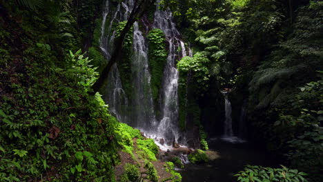 Back-view-of-woman-walking-towards-natural-pool-of-Banyu-Wana-Amertha-Waterfall,-exotic-location-in-Bali-in-Indonesia