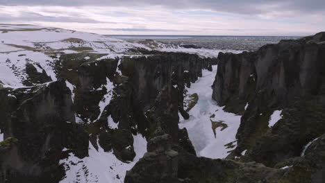 Aerial-View-of-Fjadrargljufur-Canyon,-Iceland-in-Late-WInter,-Palagonite-Rocks-and-Frozen-River,-Drone-Shot