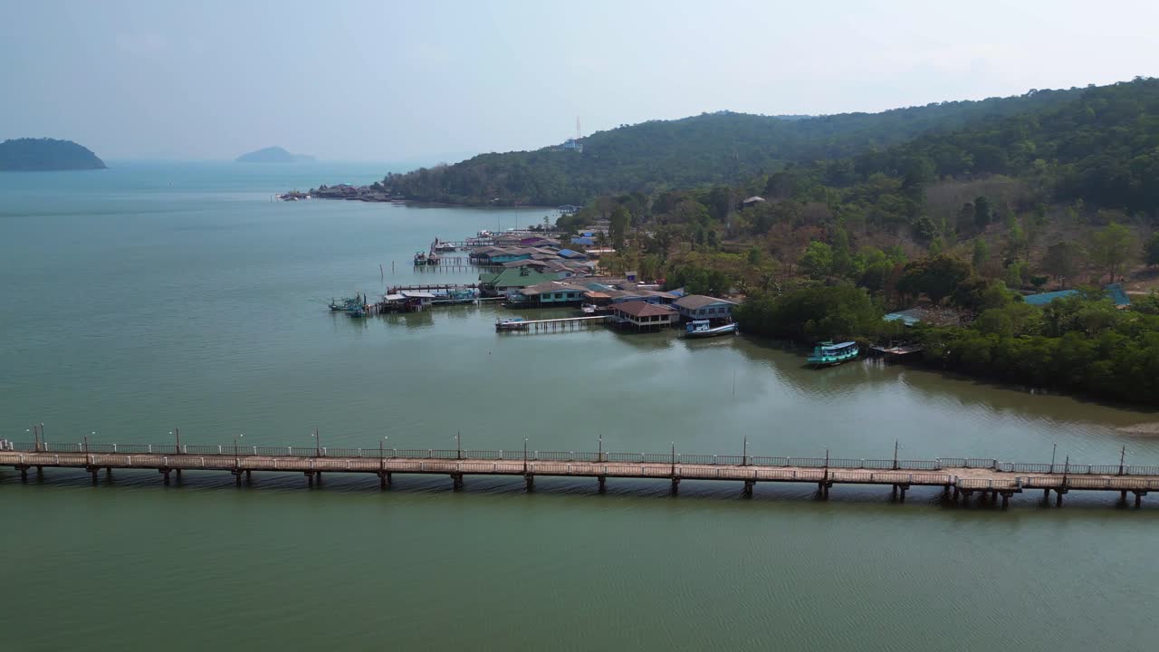 Coastal village with houses on stilts, boats and a long pier in a tropical bay. Perfect aerial view panorama orbit drone
