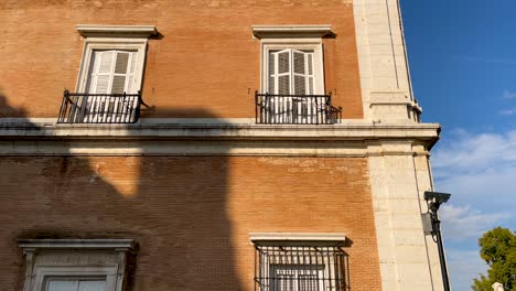 filmación de una de las esquinas del palacio real de aranjuez donde una puerta, balcones y ventanas blancas aparecen, una estatua de marmos aparece y un grupo de pájaros volando a través de la esquina de piedra blanca