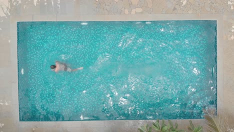 overhead-shot-of-young-fit-man-loose-casual-swimming-trunks-diving-into-small-private-home-pool