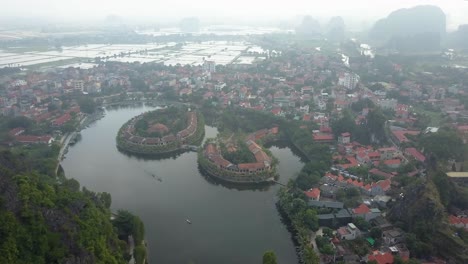 cinematic drone footage of tam coc surrounded by majestic limestone peaks in misty and foggy weather. ricefields in the wild jungle in the spring with boat tour canal in, ninh binh, vietnam