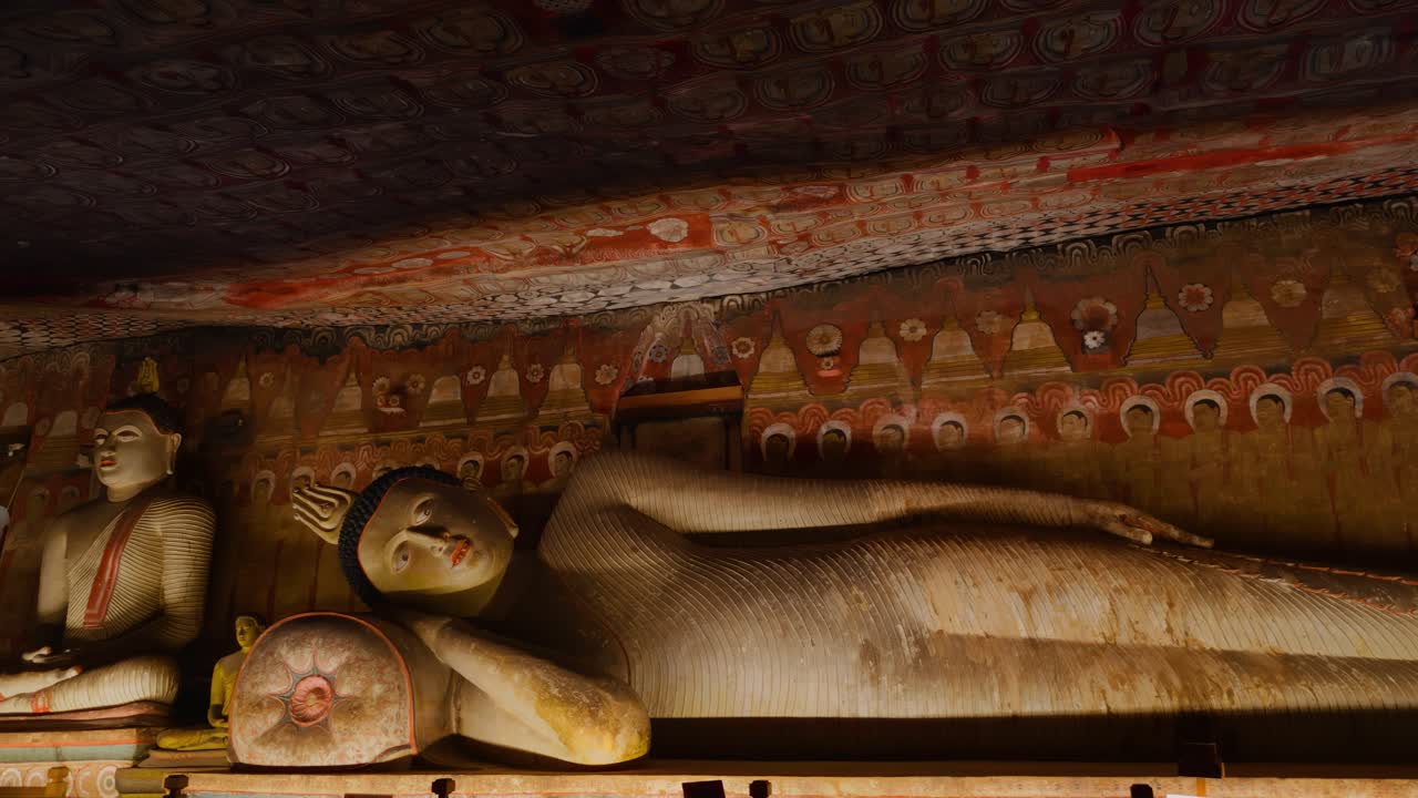 Storica statua del Buddha sdraiato e pitture murali all'interno del Tempio della Grotta di Dambulla, Provincia Centrale, Sri Lanka.