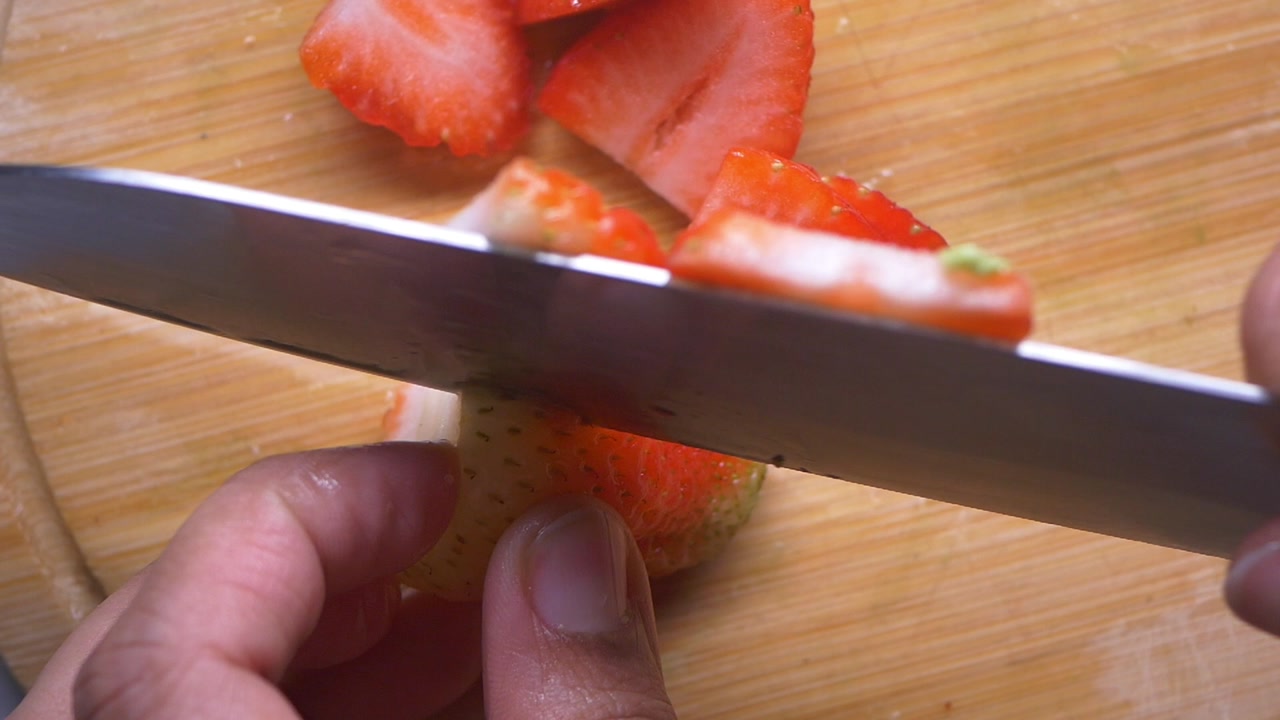 Person Slicing a Fresh Strawberry on a Wooden Cutting Board