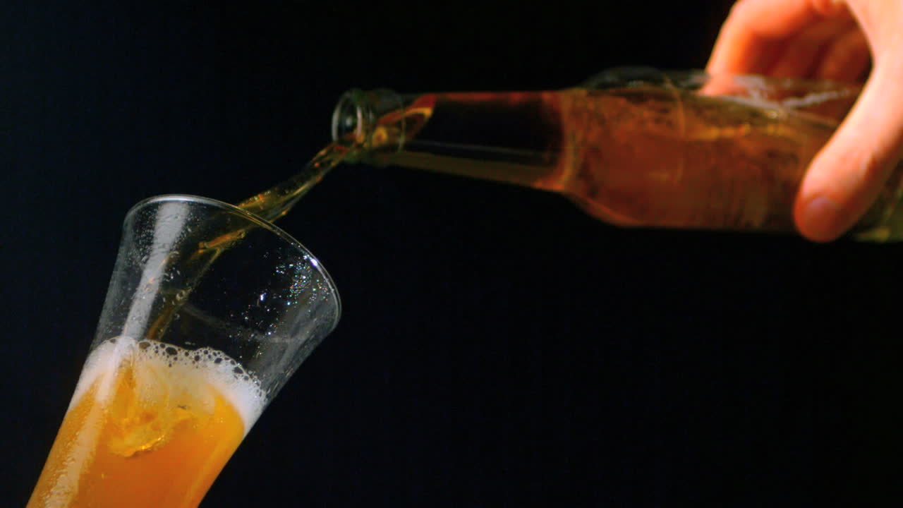 Mano che versa una bottiglia di birra in un bicchiere su sfondo nero