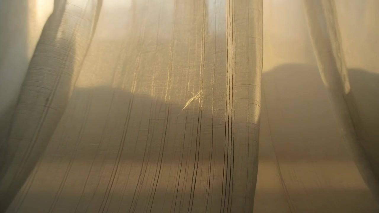 Billowing central sheer panel driven by draft from close to wide window at home, holding feather