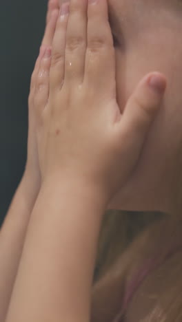 pretty small girl with long fair hair washes face with clean water in light bathroom at home close side view