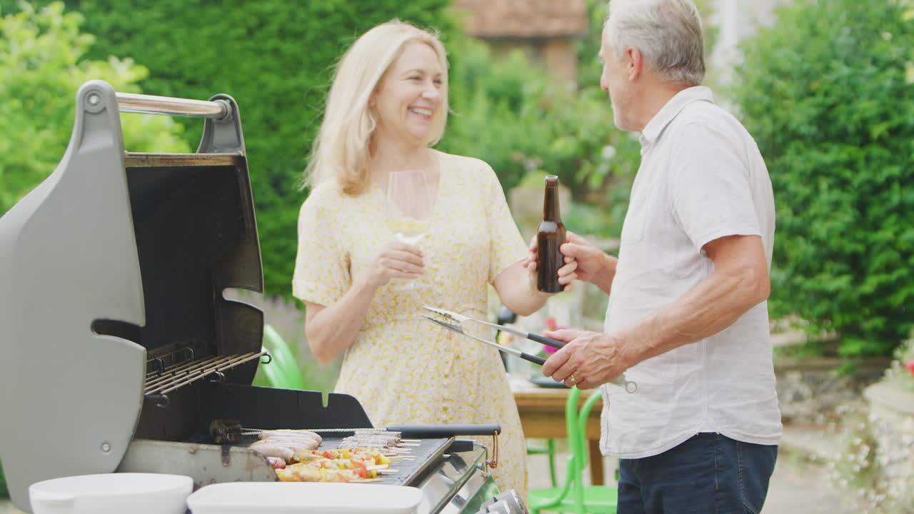 Coppia anziana che cucina un barbecue all'aperto e beve vino e birra a casa.